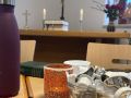 Tasse, Kaffeesahne und ein Altar mit brennenden Kerzen und Kreuz im Hinterfrund - 1. Fr&uuml;hst&uuml;cks- Gottesdienst am 25.01.2026 in Triebel