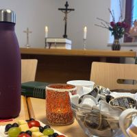 Tasse, Kaffeesahne und ein Altar mit brennenden Kerzen und Kreuz im Hinterfrund - 1. Fr&uuml;hst&uuml;cks- Gottesdienst am 25.01.2026 in Triebel