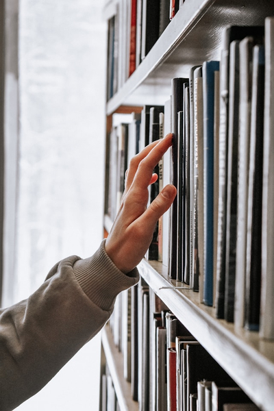 "Hilfreiches Material für Hauskreise" (Eina Hand, welche nach einem Buch in einem vollen Bücherregakl greift)