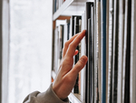"Hilfreiches Material für Hauskreise" (Eina Hand, welche nach einem Buch in einem vollen Bücherregakl greift)