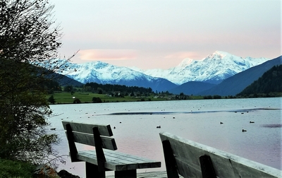 leere Parkbänke vor See mit Enten, Berge im Hintergrund