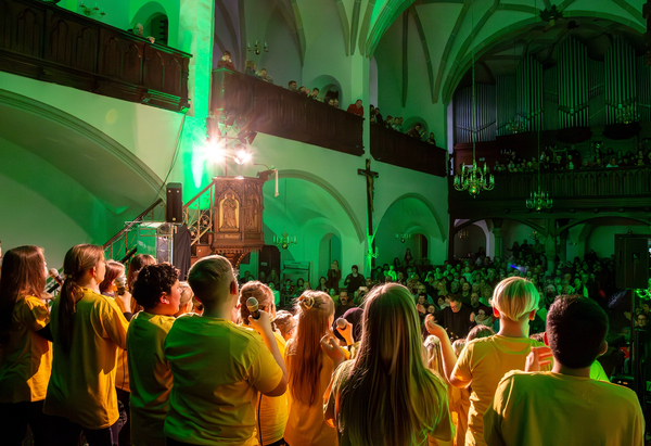 "Muscal Werkstatt 2027" (Blick über die Schulter eins Kinderchores in einem Musical in voller St. Jakobi Kirche Oelsnitz)