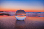 Ewigkeit (Glaskugel liegt am Strand im Sand vor einem Sonnenuntergang)